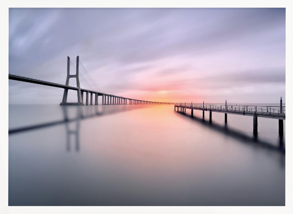 A serene long-exposure photograph of a modern cable-stayed bridge and a pier stretching over mirror-like water at sunset. The sky is filled with soft, streaky clouds in hues of pink and purple, reflected on the calm water's surface, all enclosed in a silver frame. Decor