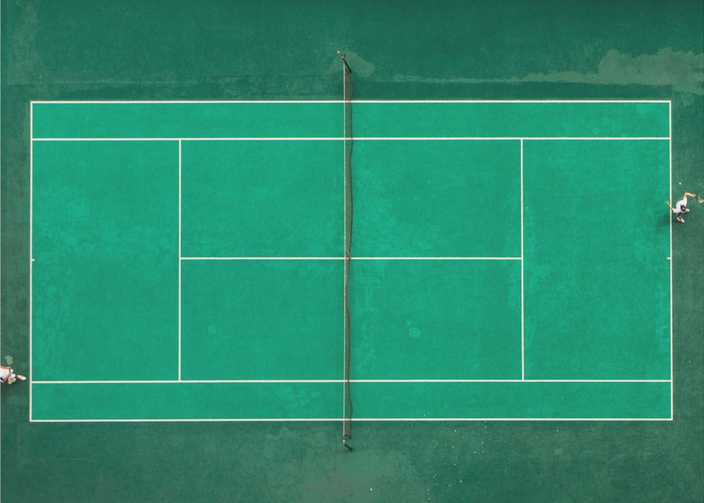 An aerial top-down photograph of a vibrant green tennis court with two players in the middle of a game, one on the far left and the other on the far right, all enclosed within a brushed silver frame. Print