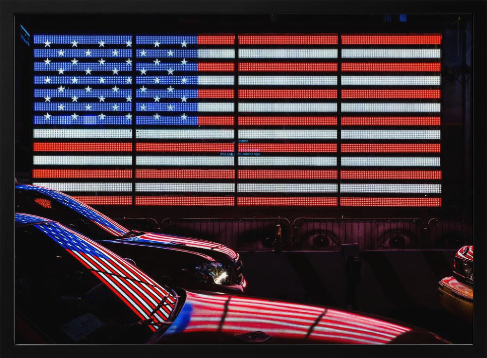 A large illuminated American flag on a billboard at night, with its red, white, and blue lights reflecting on the glossy hoods of two cars in the foreground. Wall Art