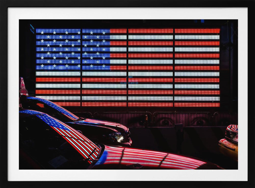 A large illuminated American flag on a billboard at night, with its red, white, and blue lights reflecting on the glossy hoods of two cars in the foreground. Wall Art