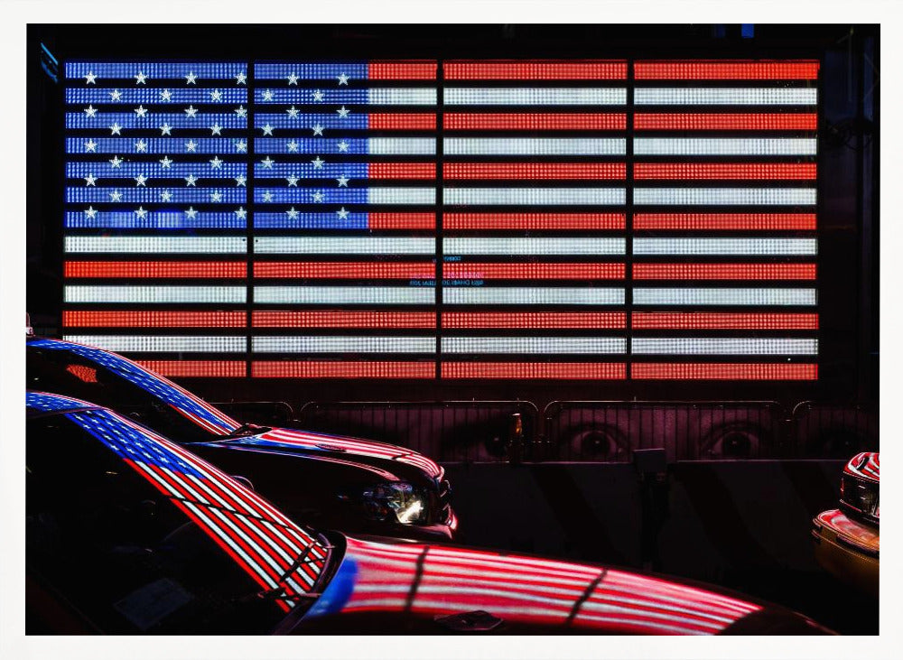 A large illuminated American flag on a billboard at night, with its red, white, and blue lights reflecting on the glossy hoods of two cars in the foreground. Wall Art