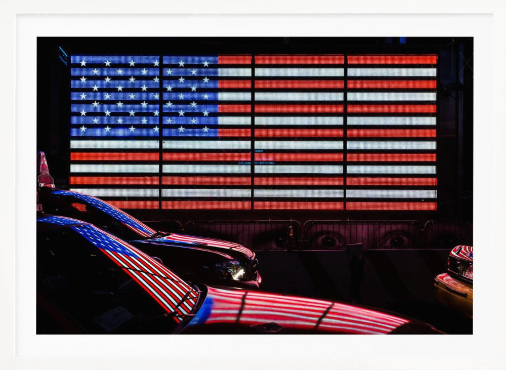 A large illuminated American flag on a billboard at night, with its red, white, and blue lights reflecting on the glossy hoods of two cars in the foreground. Wall Art