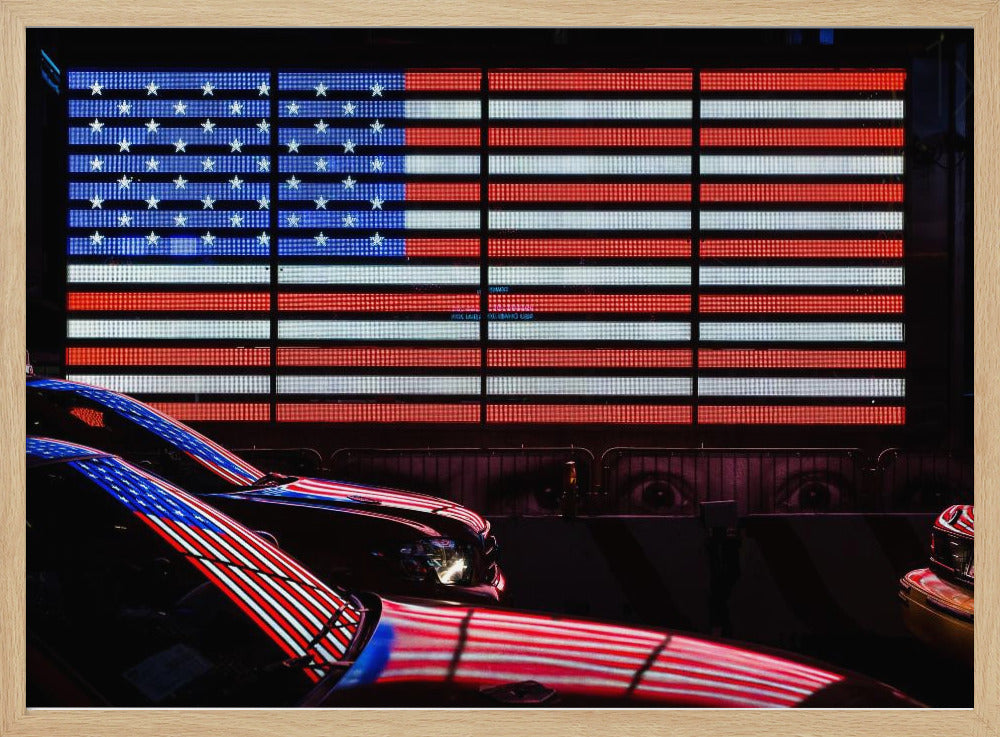 A large illuminated American flag on a billboard at night, with its red, white, and blue lights reflecting on the glossy hoods of two cars in the foreground. Wall Art