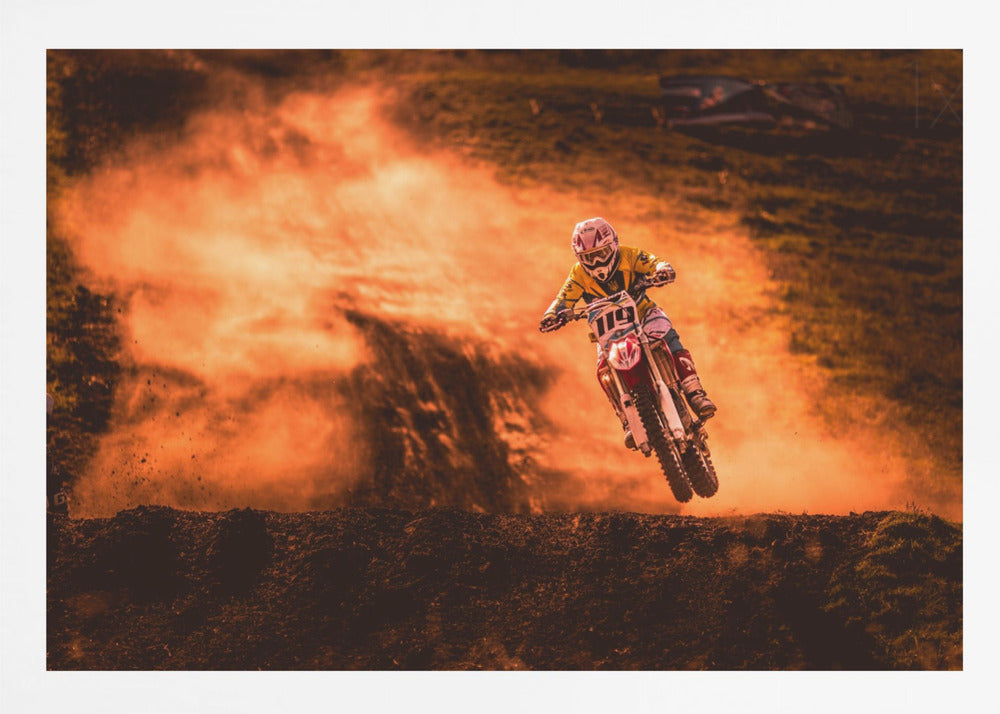 An action-packed photo of a motocross rider in mid-air, jumping their dirt bike over a mound of earth. A large cloud of orange dust billows behind them, creating a dramatic and fiery background. Wall Art