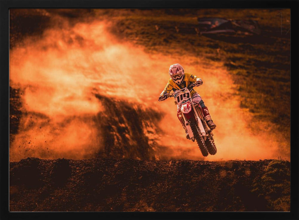 An action-packed photo of a motocross rider in mid-air, jumping their dirt bike over a mound of earth. A large cloud of orange dust billows behind them, creating a dramatic and fiery background. Wall Art