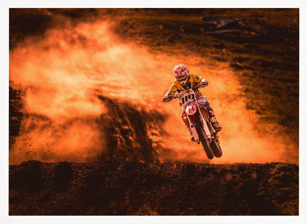 An action-packed photo of a motocross rider in mid-air, jumping their dirt bike over a mound of earth. A large cloud of orange dust billows behind them, creating a dramatic and fiery background. Wall Art