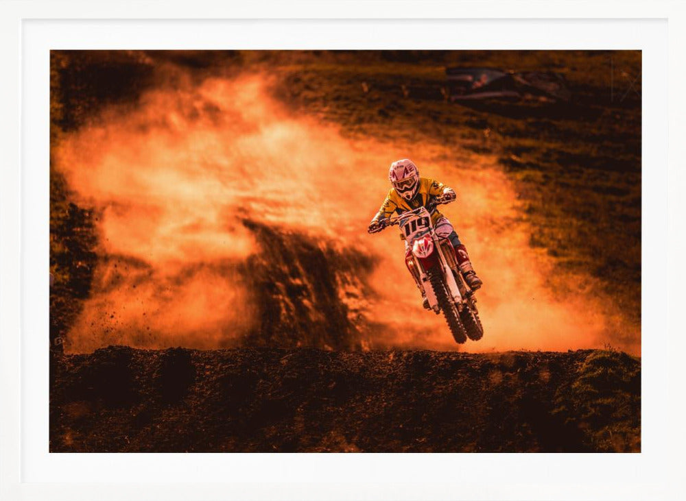 An action-packed photo of a motocross rider in mid-air, jumping their dirt bike over a mound of earth. A large cloud of orange dust billows behind them, creating a dramatic and fiery background. Wall Art
