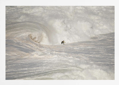A framed photograph of a lone surfer dwarfed by a massive, powerful ocean wave. The water is a churning mass of white foam and spray, and the surfer is navigating the enormous swell. Print