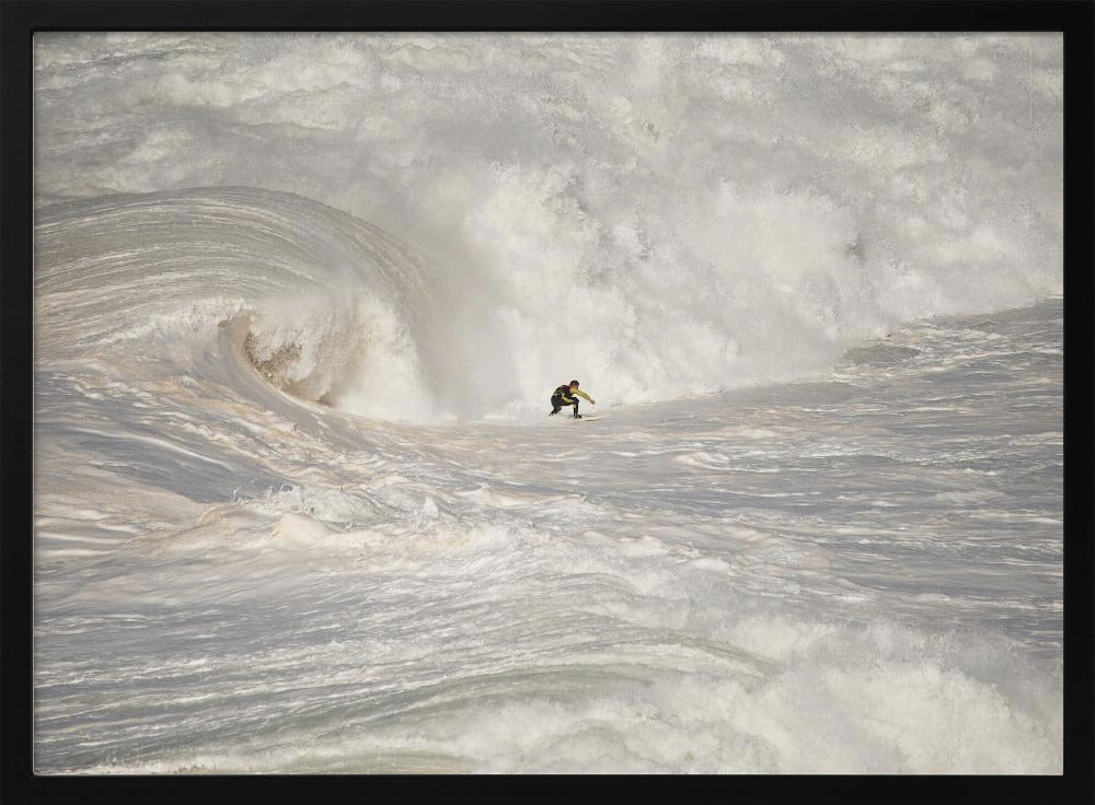 A framed photograph of a lone surfer dwarfed by a massive, powerful ocean wave. The water is a churning mass of white foam and spray, and the surfer is navigating the enormous swell. Print
