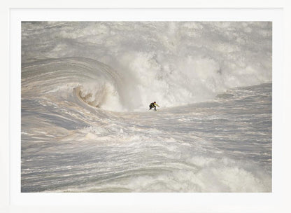 A framed photograph of a lone surfer dwarfed by a massive, powerful ocean wave. The water is a churning mass of white foam and spray, and the surfer is navigating the enormous swell. Print