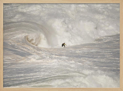 A framed photograph of a lone surfer dwarfed by a massive, powerful ocean wave. The water is a churning mass of white foam and spray, and the surfer is navigating the enormous swell. Print