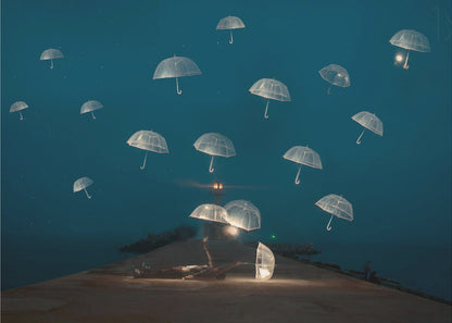 A surreal night scene with a person lying on a pier next to a glowing, transparent umbrella, while numerous other glowing umbrellas float like jellyfish in the dark blue sky above the sea, with a distant lighthouse in the background. Poster