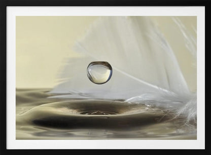 A high-speed macro photograph captures a perfectly spherical water droplet suspended in mid-air above a ripple on the water's surface. A soft white feather lies in the background, creating a serene and delicate composition with a neutral color palette, all enclosed in a brushed silver frame. Wall Art