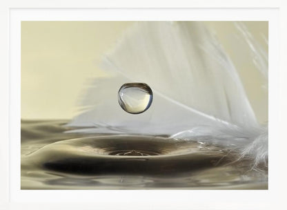 A high-speed macro photograph captures a perfectly spherical water droplet suspended in mid-air above a ripple on the water's surface. A soft white feather lies in the background, creating a serene and delicate composition with a neutral color palette, all enclosed in a brushed silver frame. Wall Art