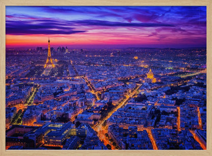 An aerial panoramic view of Paris at dusk, with the cityscape illuminated in cool blue and warm yellow lights. The Eiffel Tower is prominently lit on the left under a dramatic sunset sky transitioning from orange and pink to deep purple. Poster