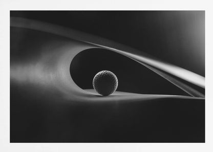 An artistic black and white photograph of a golf ball resting inside the gentle curve of a dark, abstract shape, creating a minimalist and dramatic composition with strong light and shadows. Poster