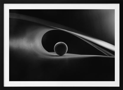 An artistic black and white photograph of a golf ball resting inside the gentle curve of a dark, abstract shape, creating a minimalist and dramatic composition with strong light and shadows. Poster