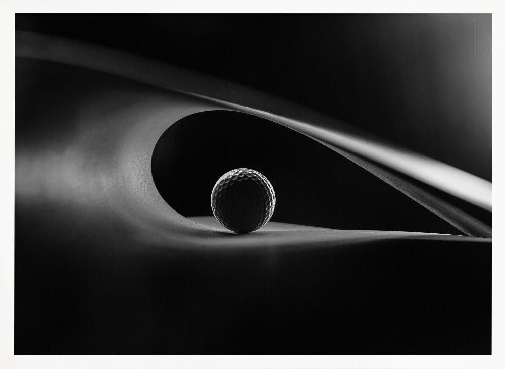 An artistic black and white photograph of a golf ball resting inside the gentle curve of a dark, abstract shape, creating a minimalist and dramatic composition with strong light and shadows. Poster