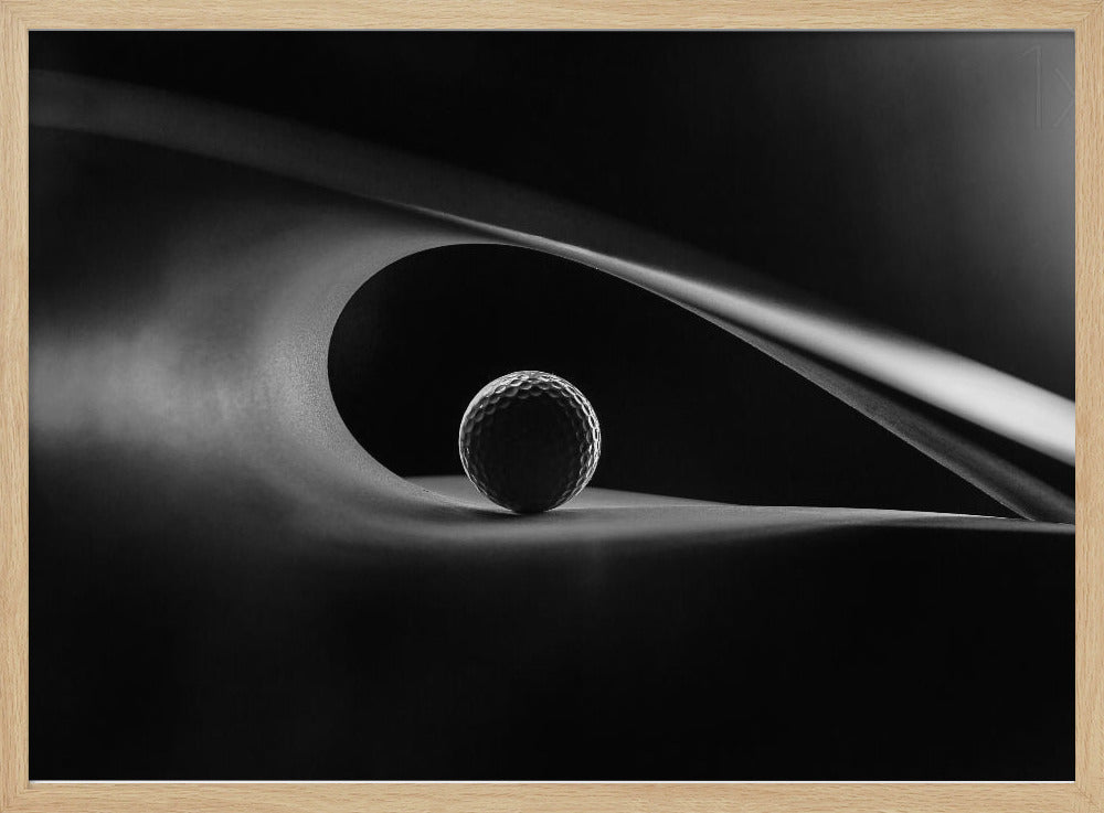 An artistic black and white photograph of a golf ball resting inside the gentle curve of a dark, abstract shape, creating a minimalist and dramatic composition with strong light and shadows. Poster