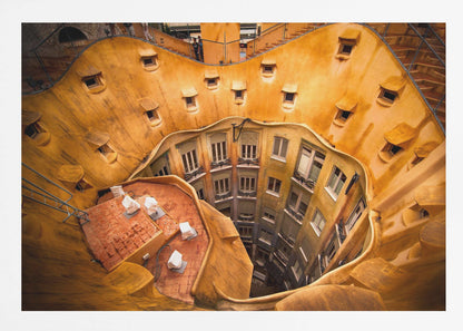 A high-angle photograph looking down into the surreal, undulating inner courtyard of an architectural masterpiece. The warm, golden-ochre walls curve organically, dotted with small, hooded windows, encircling the deep central lightwell that reveals floors of apartments below. Wall Art