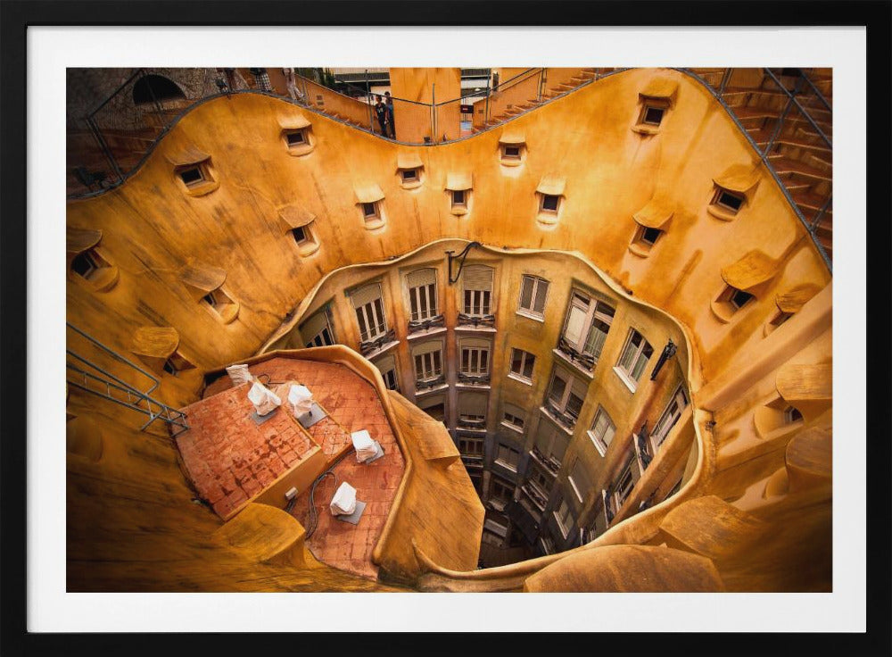 A high-angle photograph looking down into the surreal, undulating inner courtyard of an architectural masterpiece. The warm, golden-ochre walls curve organically, dotted with small, hooded windows, encircling the deep central lightwell that reveals floors of apartments below. Wall Art