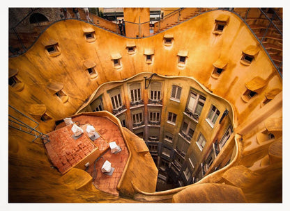A high-angle photograph looking down into the surreal, undulating inner courtyard of an architectural masterpiece. The warm, golden-ochre walls curve organically, dotted with small, hooded windows, encircling the deep central lightwell that reveals floors of apartments below. Wall Art