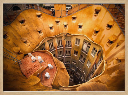 A high-angle photograph looking down into the surreal, undulating inner courtyard of an architectural masterpiece. The warm, golden-ochre walls curve organically, dotted with small, hooded windows, encircling the deep central lightwell that reveals floors of apartments below. Wall Art