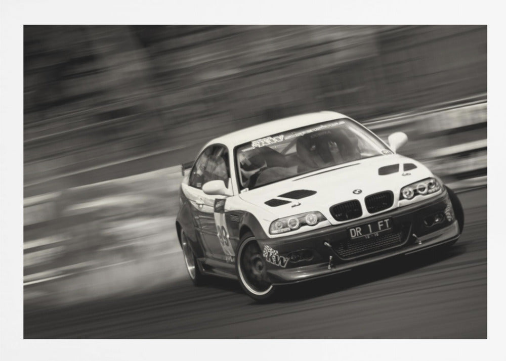 A framed, black and white action photograph of a white and black BMW race car drifting at high speed around a corner. The background is blurred with motion lines, emphasizing the car's speed as it turns, and a puff of smoke is visible from the tires. Wall Art
