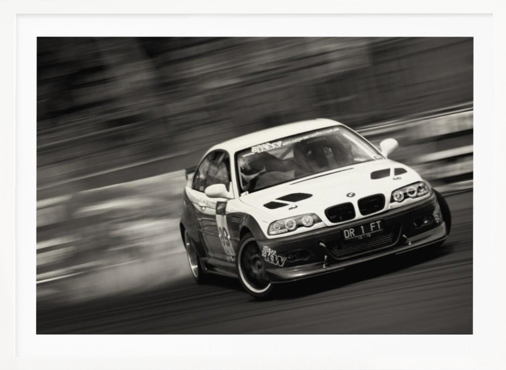 A framed, black and white action photograph of a white and black BMW race car drifting at high speed around a corner. The background is blurred with motion lines, emphasizing the car's speed as it turns, and a puff of smoke is visible from the tires. Wall Art