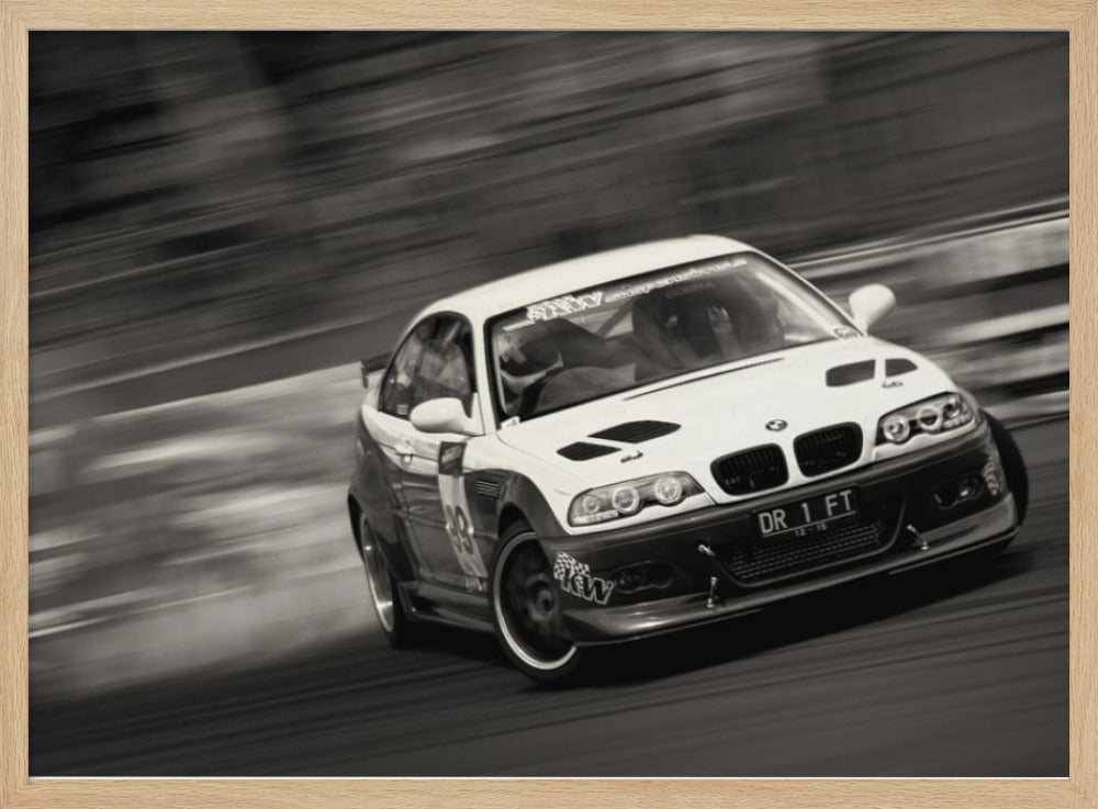 A framed, black and white action photograph of a white and black BMW race car drifting at high speed around a corner. The background is blurred with motion lines, emphasizing the car's speed as it turns, and a puff of smoke is visible from the tires. Wall Art