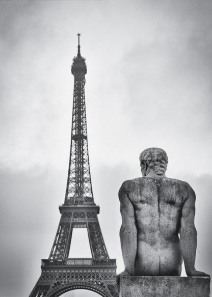 A black and white photograph capturing a contemplative scene in Paris, with the back of a seated, muscular male stone statue in the foreground looking towards the iconic Eiffel Tower which stands tall against a cloudy sky. Print