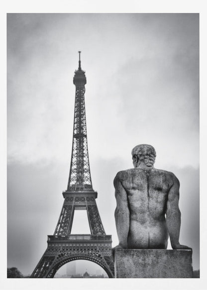 A black and white photograph capturing a contemplative scene in Paris, with the back of a seated, muscular male stone statue in the foreground looking towards the iconic Eiffel Tower which stands tall against a cloudy sky. Print