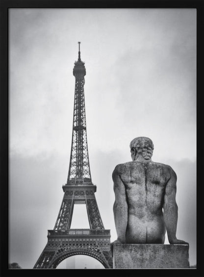 A black and white photograph capturing a contemplative scene in Paris, with the back of a seated, muscular male stone statue in the foreground looking towards the iconic Eiffel Tower which stands tall against a cloudy sky. Print