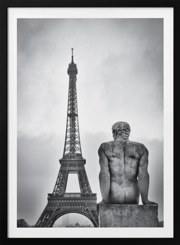 A black and white photograph capturing a contemplative scene in Paris, with the back of a seated, muscular male stone statue in the foreground looking towards the iconic Eiffel Tower which stands tall against a cloudy sky. Print