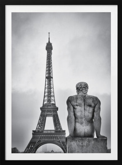 A black and white photograph capturing a contemplative scene in Paris, with the back of a seated, muscular male stone statue in the foreground looking towards the iconic Eiffel Tower which stands tall against a cloudy sky. Print