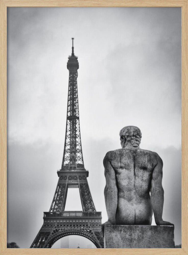 A black and white photograph capturing a contemplative scene in Paris, with the back of a seated, muscular male stone statue in the foreground looking towards the iconic Eiffel Tower which stands tall against a cloudy sky. Print
