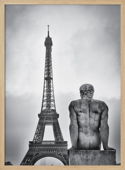 A black and white photograph capturing a contemplative scene in Paris, with the back of a seated, muscular male stone statue in the foreground looking towards the iconic Eiffel Tower which stands tall against a cloudy sky. Print