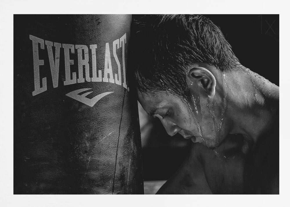 A dramatic black and white close-up photograph of an exhausted boxer resting his head against a heavy Everlast punching bag, with sweat dripping down his face and neck. Poster
