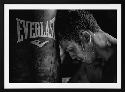 A dramatic black and white close-up photograph of an exhausted boxer resting his head against a heavy Everlast punching bag, with sweat dripping down his face and neck. Poster