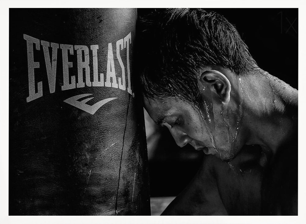 A dramatic black and white close-up photograph of an exhausted boxer resting his head against a heavy Everlast punching bag, with sweat dripping down his face and neck. Poster