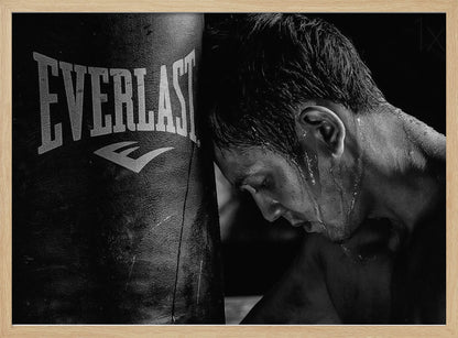 A dramatic black and white close-up photograph of an exhausted boxer resting his head against a heavy Everlast punching bag, with sweat dripping down his face and neck. Poster