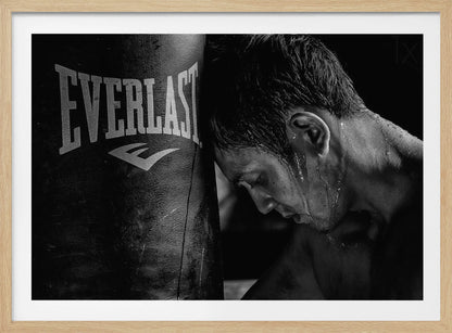 A dramatic black and white close-up photograph of an exhausted boxer resting his head against a heavy Everlast punching bag, with sweat dripping down his face and neck. Poster