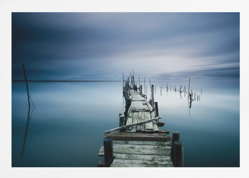 A framed, long exposure photograph of a weathered wooden pier extending into calm, misty blue water under a dramatic, cloudy sky. Wall Art