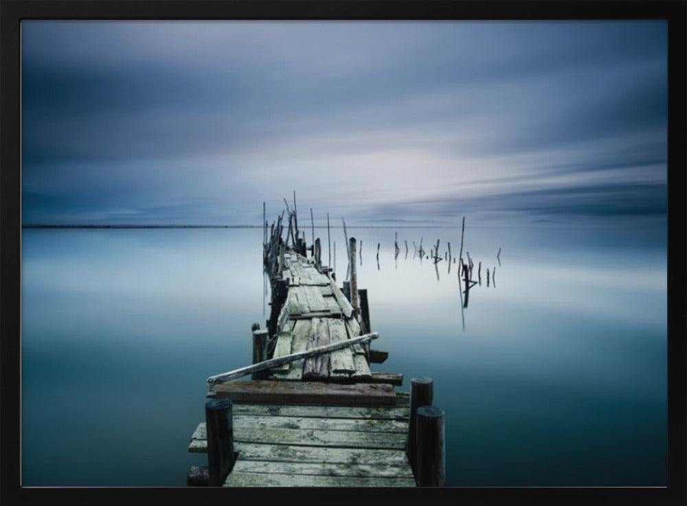 A framed, long exposure photograph of a weathered wooden pier extending into calm, misty blue water under a dramatic, cloudy sky. Wall Art