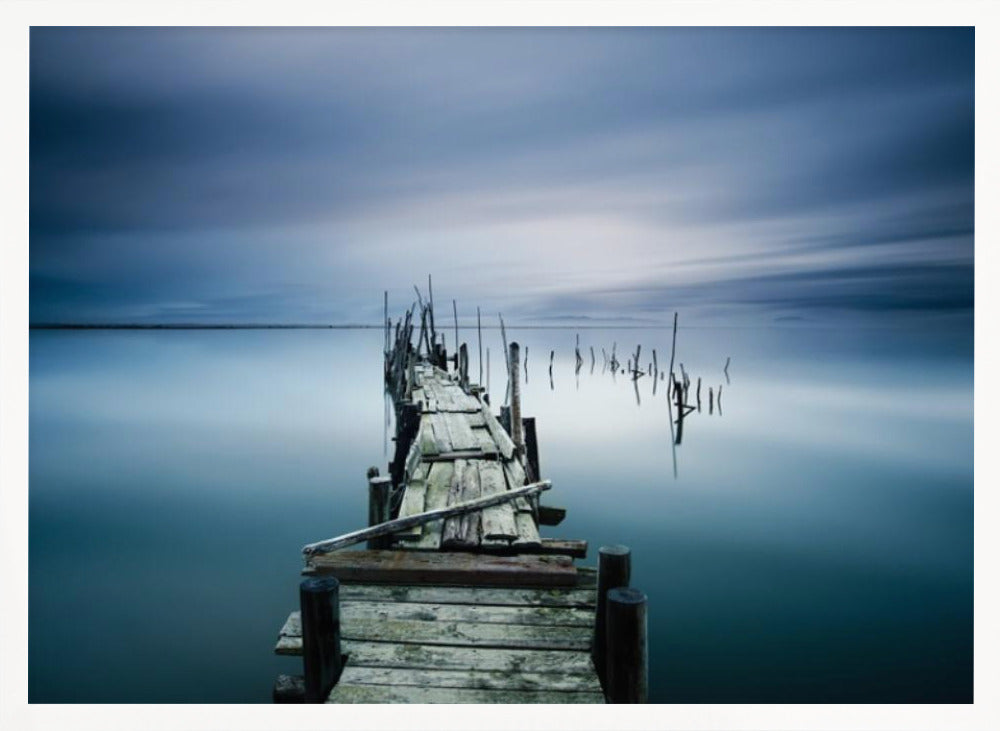 A framed, long exposure photograph of a weathered wooden pier extending into calm, misty blue water under a dramatic, cloudy sky. Wall Art