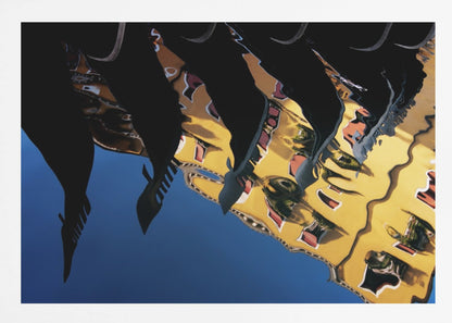 An abstract photograph of a distorted reflection in water, showing a vibrant yellow building against a deep blue sky, with the dark silhouettes of several Venetian gondola prows cutting across the top of the image. The entire scene is enclosed in a silver picture frame. Print