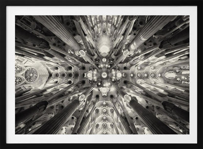 A framed black and white photograph captures the breathtaking, symmetrical ceiling of Gaudí's Sagrada Familia basilica, viewed directly from below. The massive columns rise and branch out like a forest canopy, creating a complex and mesmerizing architectural pattern of vaults, ribs, and skylights. Artwork