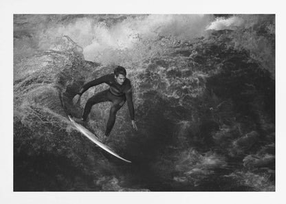A dramatic black and white photograph of a surfer in a wetsuit skillfully riding down the face of a large, turbulent wave. The image is enclosed in a silver frame. Wall Art
