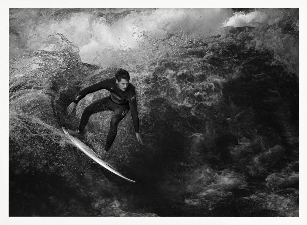 A dramatic black and white photograph of a surfer in a wetsuit skillfully riding down the face of a large, turbulent wave. The image is enclosed in a silver frame. Wall Art