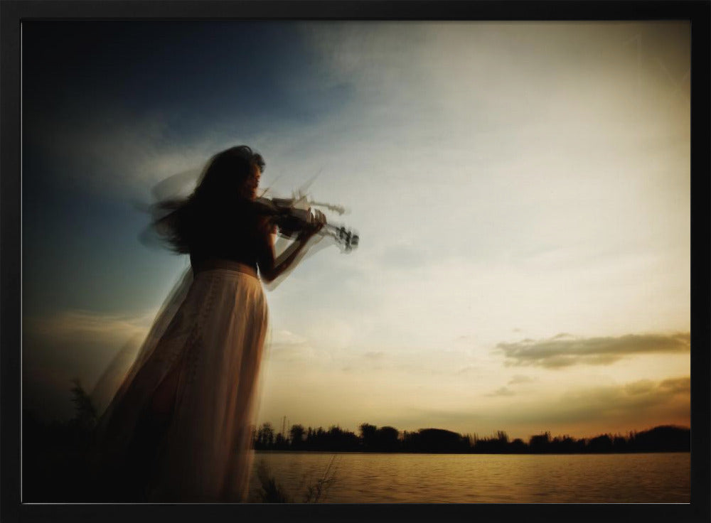 An artistic, framed photograph with motion blur capturing the silhouette of a woman in a long flowing skirt playing the violin by a lake against a dramatic sunset sky. Poster